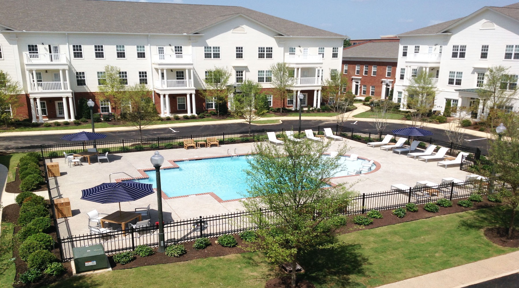 wide view of pool area showing nearness to property, reclining seats and surrounding green turf walk areas